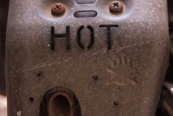 Metal heat shield covering a muffler stamped with hot and a hand indicating do not touch