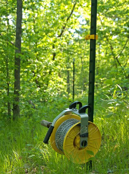 Polywire fence and reel installed on metal posts and running through pasture woods