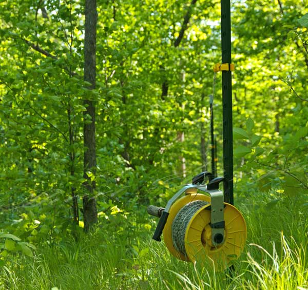Polywire fence and reel installed on metal posts and running through pasture woods