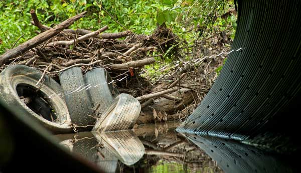 Tires and branches blocking the flow of a drainage tinhorn, Tires in a creek