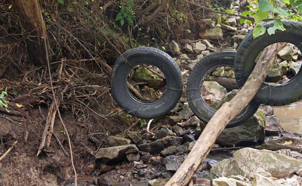 Old tires, suspended by wire and cable, in a water gap being used to contain cattle.  Cattle fencing.  Cattle panel suspended across a water gap used to contain cattle.