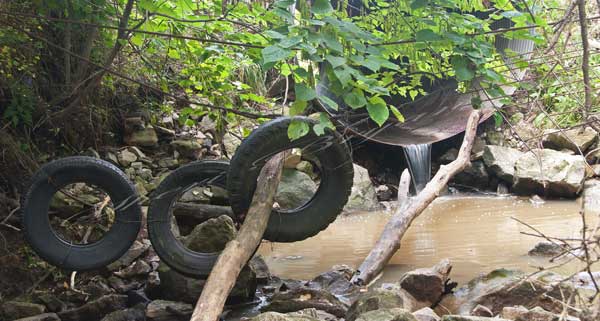 Old tires, suspended by wire and cable, in a water gap being used to contain cattle.  Cattle fencing.  Cattle panel suspended across a water gap used to contain cattle.